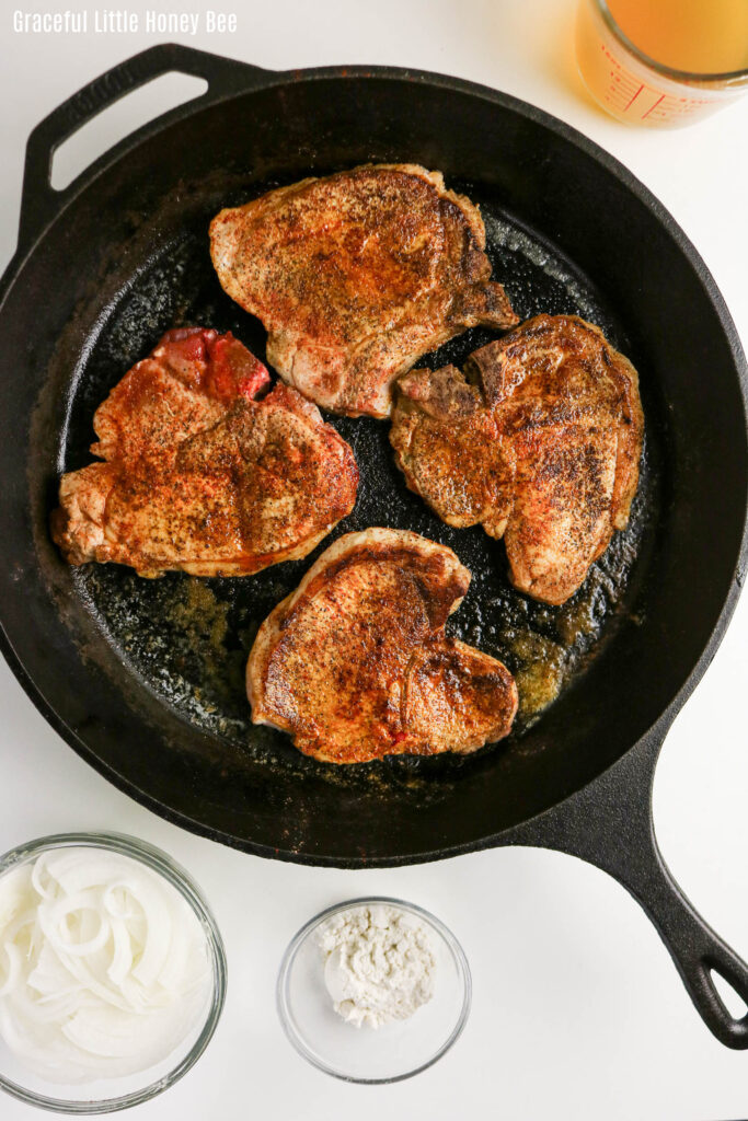 Four browned pork chops in a cast iron pan.