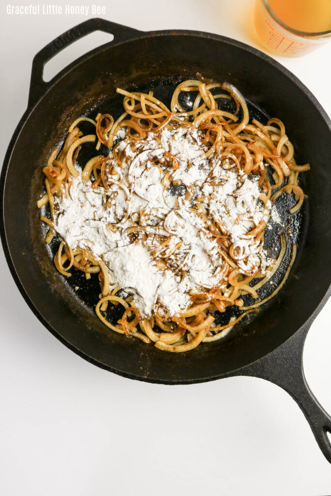 Cooked onions sprinkled with flour in a cast iron pan.