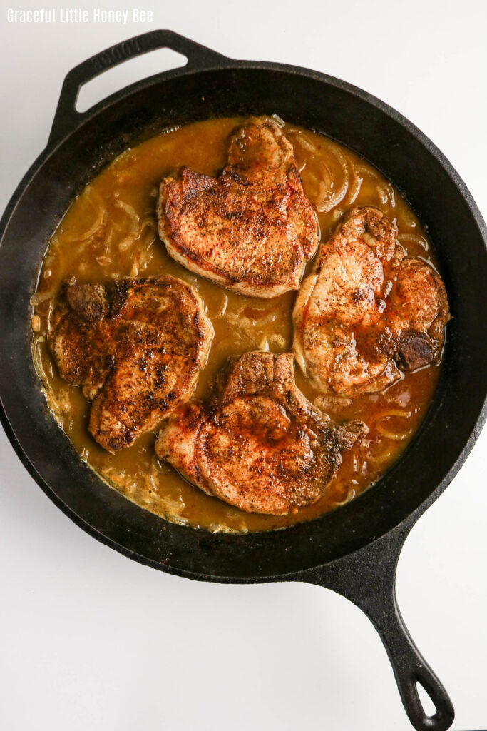 Aerial view of four pork chops smothered in onion gravy in a cast iron pan.