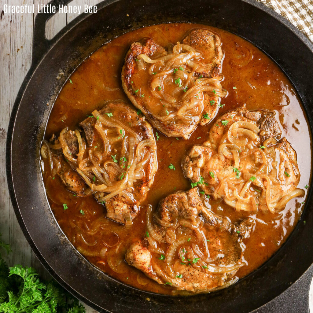 Four smothered pork chops in a cast iron pan with onion gravy.