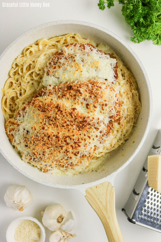 Alfredo drenched noodles topped with crisp pieces of chicken with cheese melted on top in a pot.