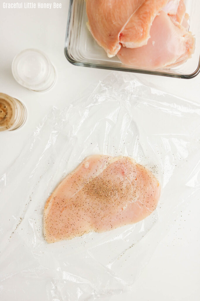 Thin chicken breast inbetween plastic wrap.