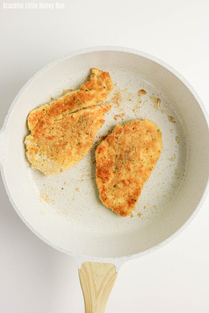 Two thin crispy pieces of chicken in a frying pan.
