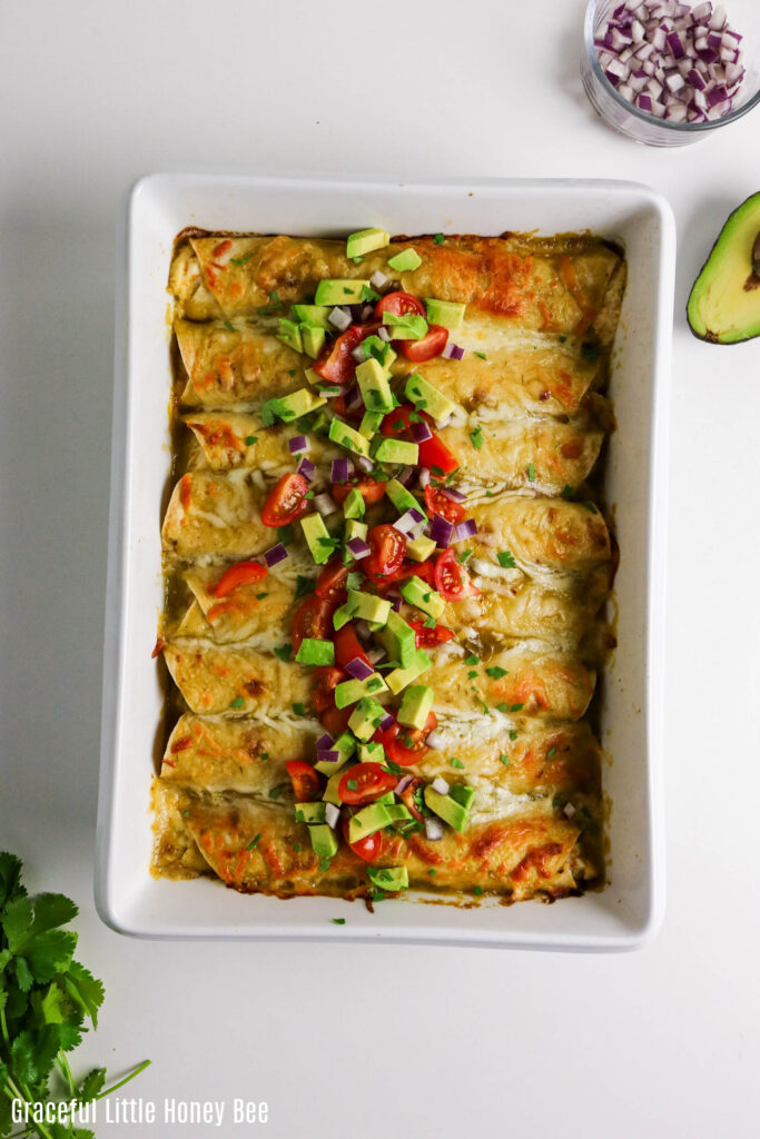 Top view of pan of chicken enchiladas topped with avocado and diced tomatoes.