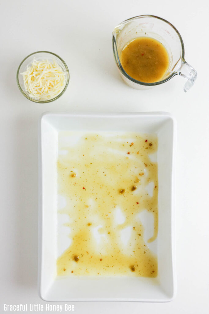 White casserole dish with a drizzle of enchilada sauce on the bottom of the pan.
