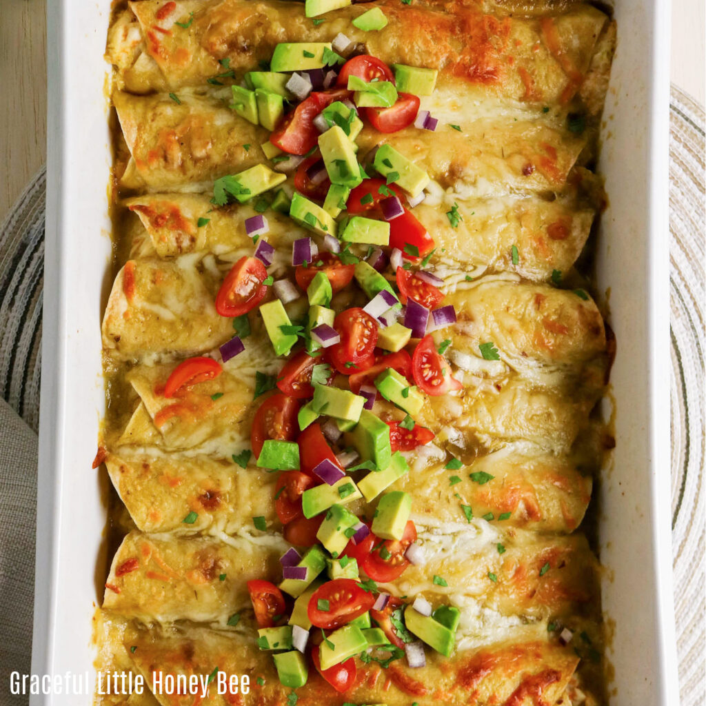 Top view of pan of chicken enchiladas topped with avocado and diced tomatoes.